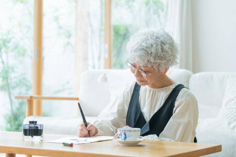 自宅で書き物をする高齢女性