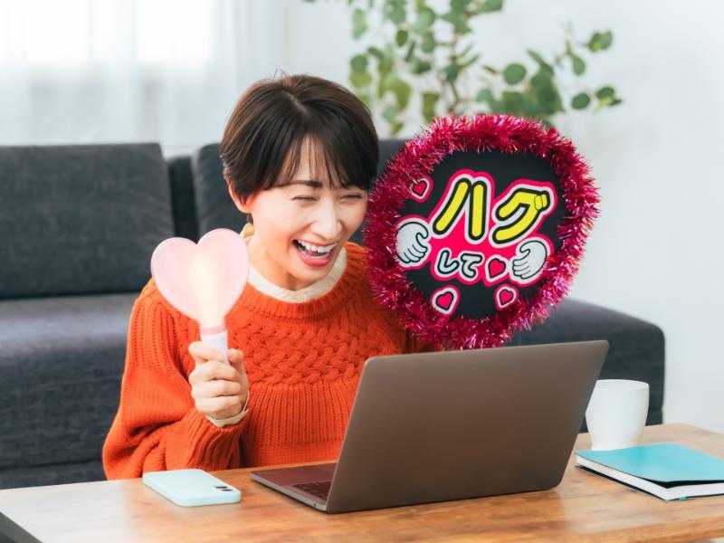 PCの前でペンライトとうちわを持って推し活する女性
