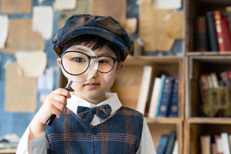 虫眼鏡を通してこちらを見る探偵のような服を着た子供
